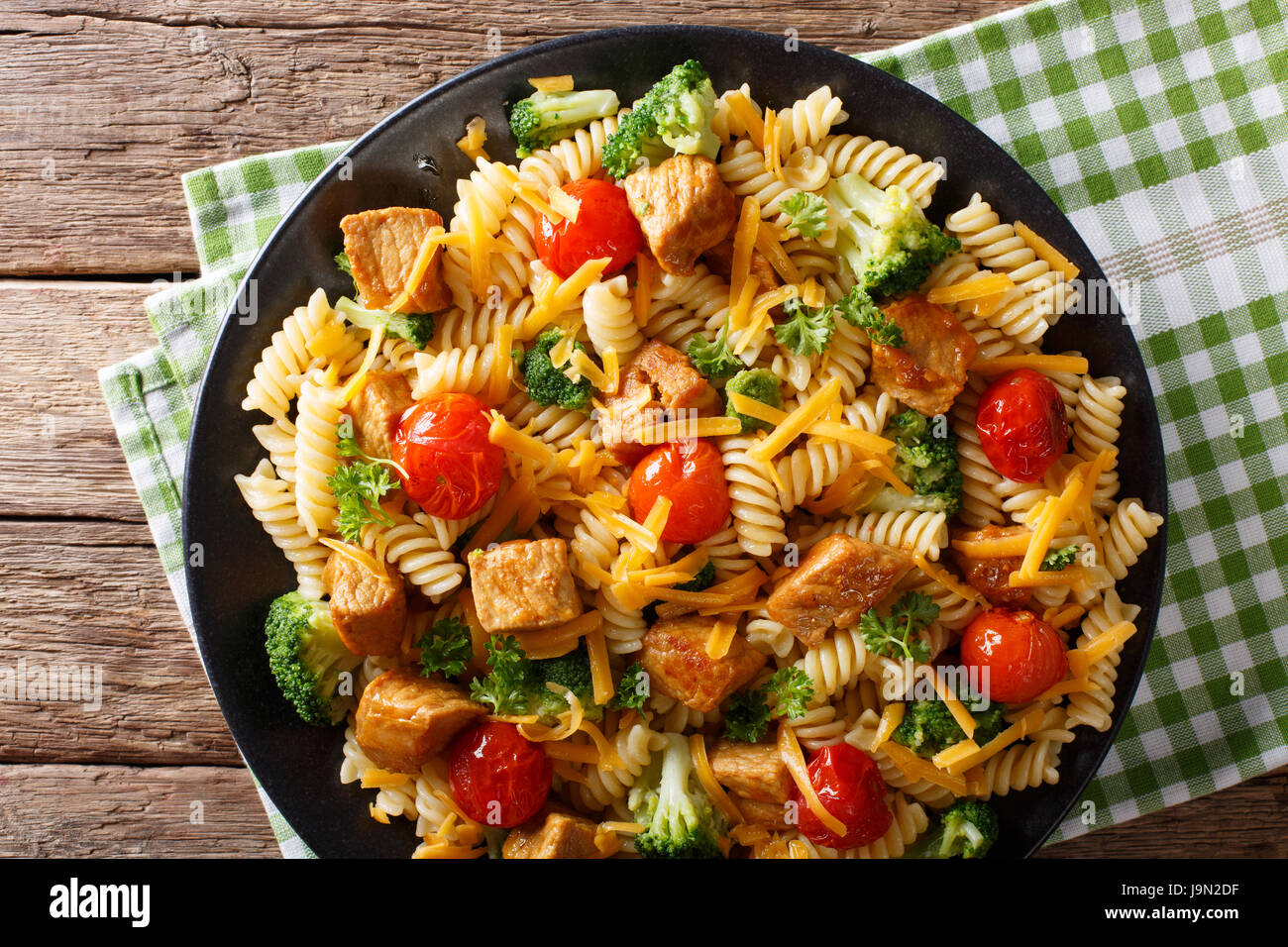 Italian fusilli con carne di maiale, broccoli, i pomodori e il formaggio cheddar vicino sul tavolo. vista orizzontale dal di sopra Foto Stock