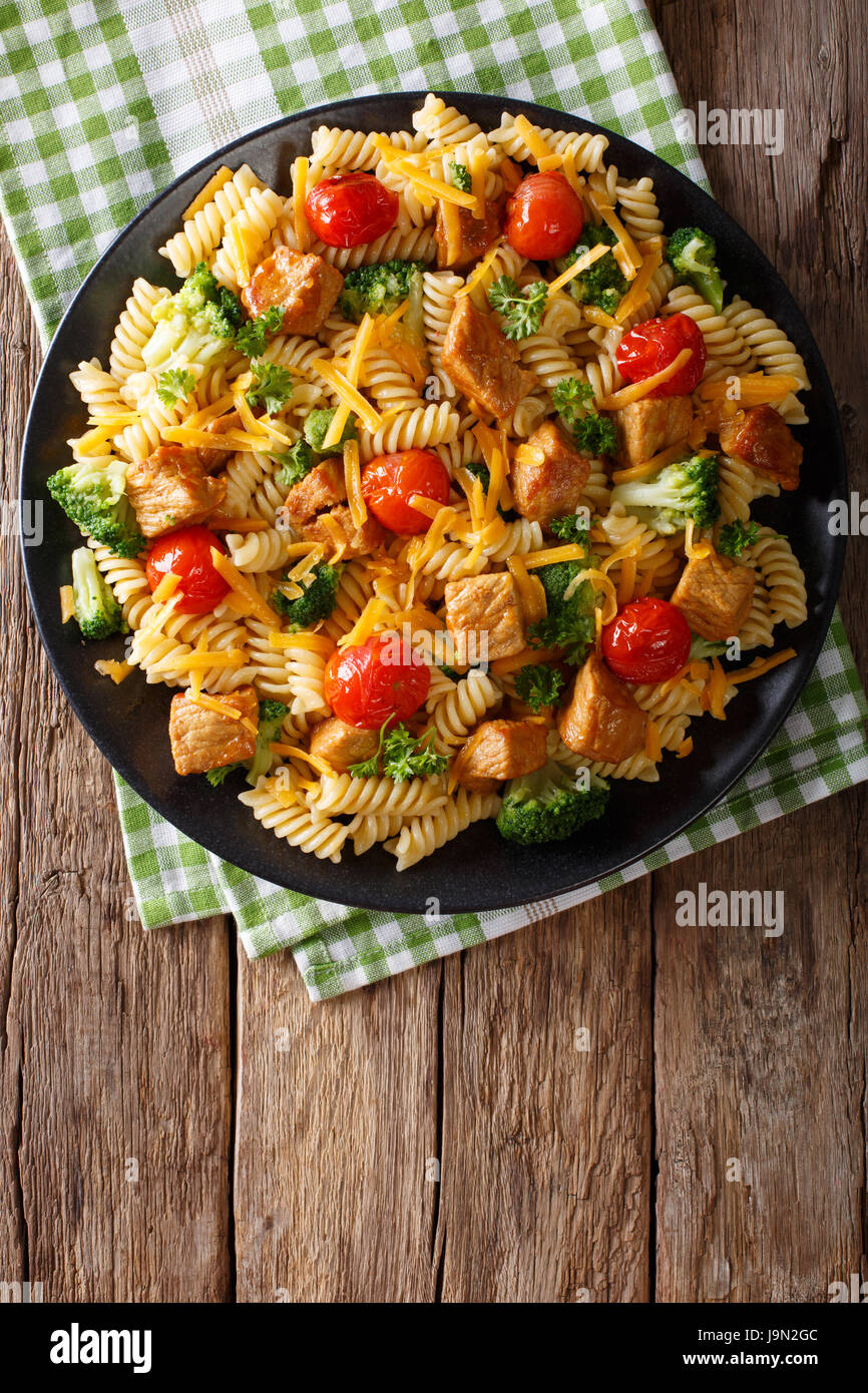 Fusilli con carne di maiale, broccoli, i pomodori e il formaggio cheddar vicino sul tavolo. Vista verticale da sopra Foto Stock