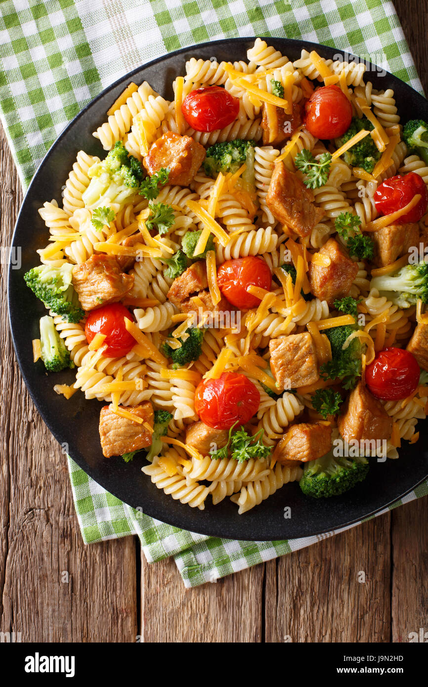 Italian fusilli con carne di maiale, broccoli, i pomodori e il formaggio cheddar vicino sul tavolo. vista orizzontale dal di sopra Foto Stock