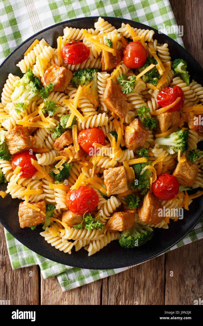 Pasta fusilli con carne di maiale, broccoli, i pomodori e il formaggio cheddar macro su una piastra. Vista verticale da sopra Foto Stock