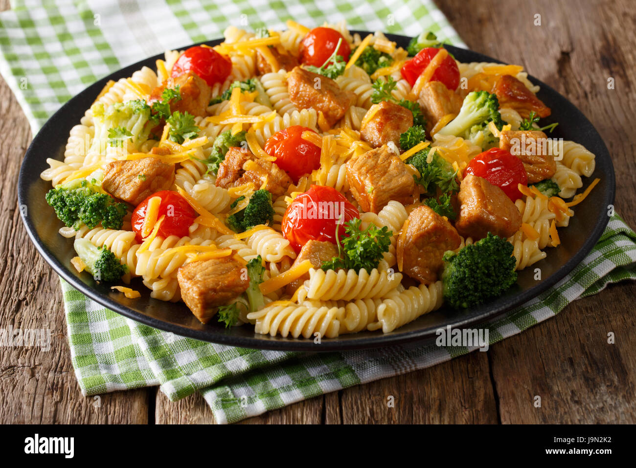 Fusilli con carne di maiale piccante, broccoli, i pomodori e il formaggio cheddar close-up su una piastra orizzontale. Foto Stock