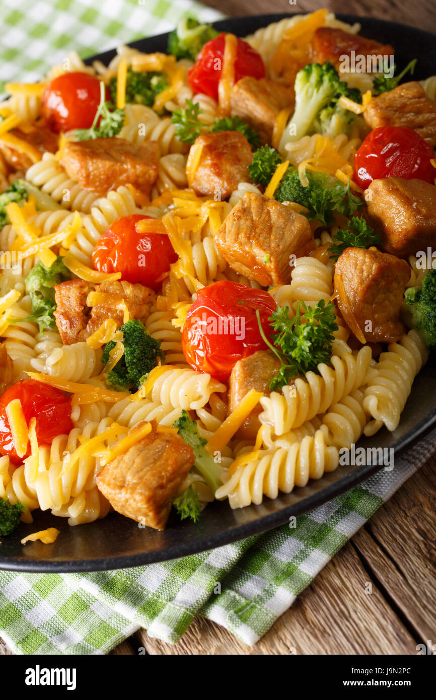 Fusilli con carne di maiale piccante, broccoli, i pomodori e il formaggio cheddar close-up su una piastra. In verticale Foto Stock