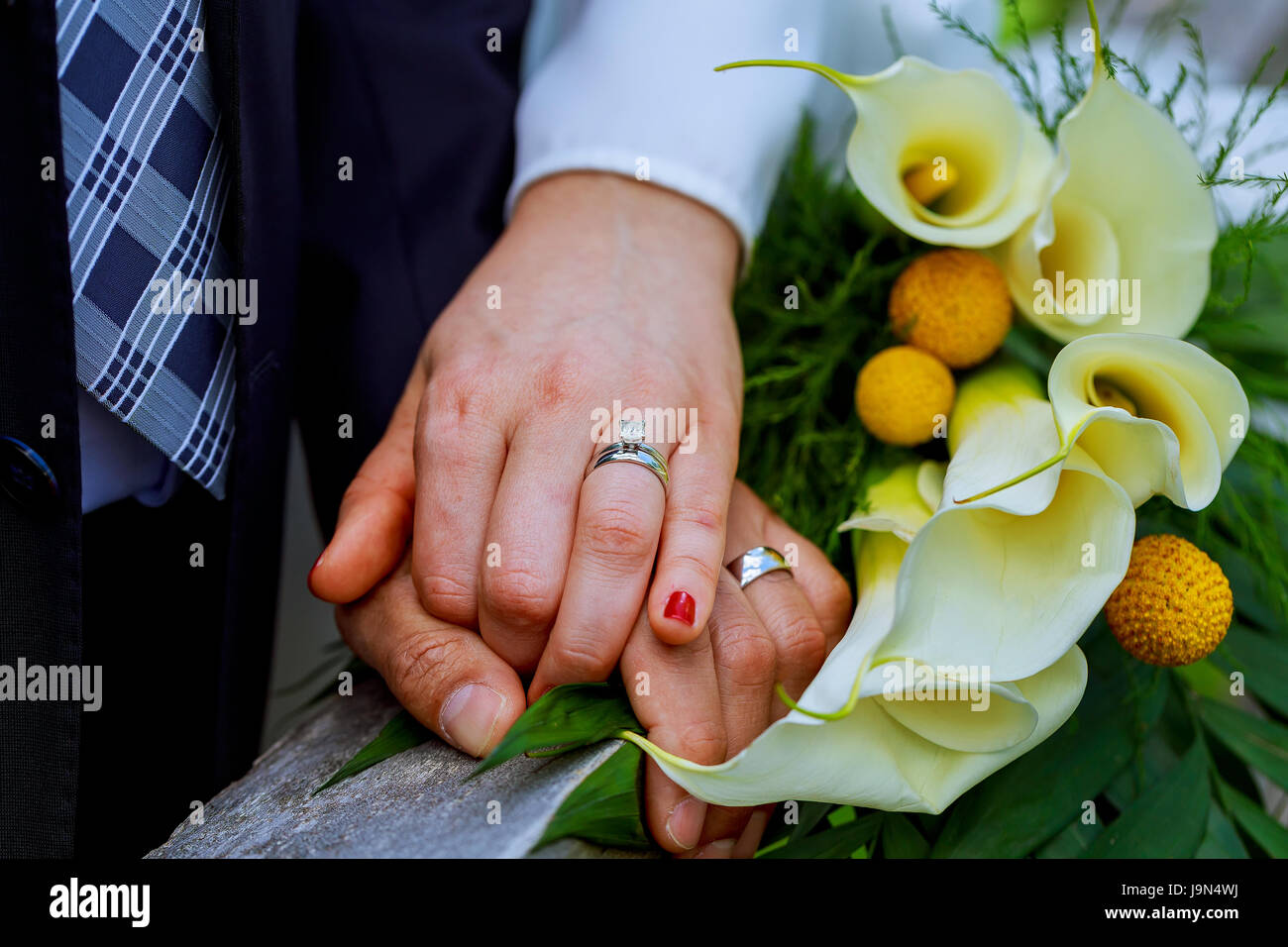 Mani con il matrimonio gli anelli in oro happy sposi novelli e bouquet di fiori kala Foto Stock