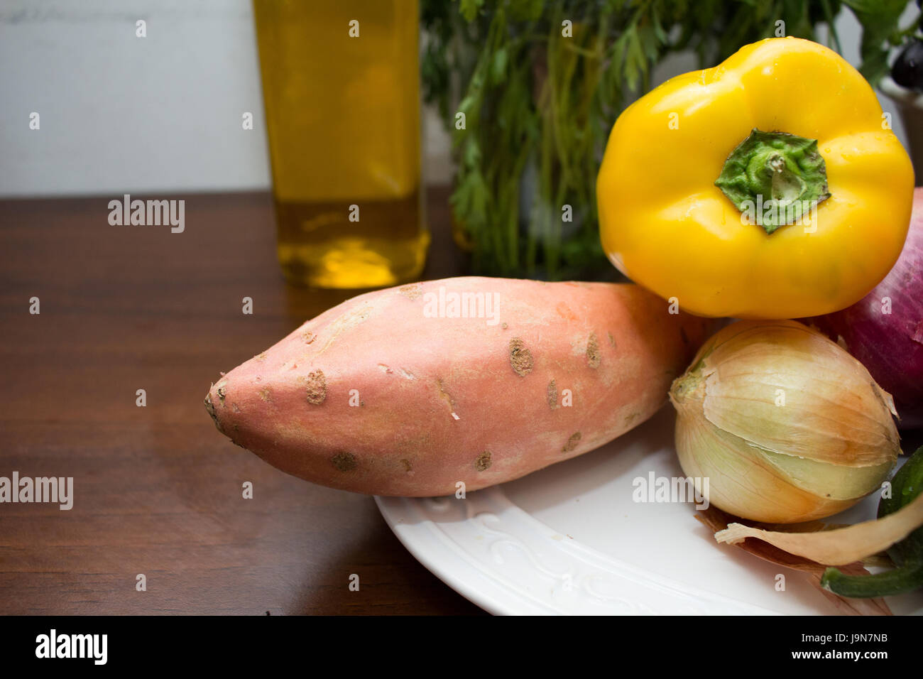 La patata dolce, il peperone giallo e le cipolle su una piastra su un tavolo Foto Stock