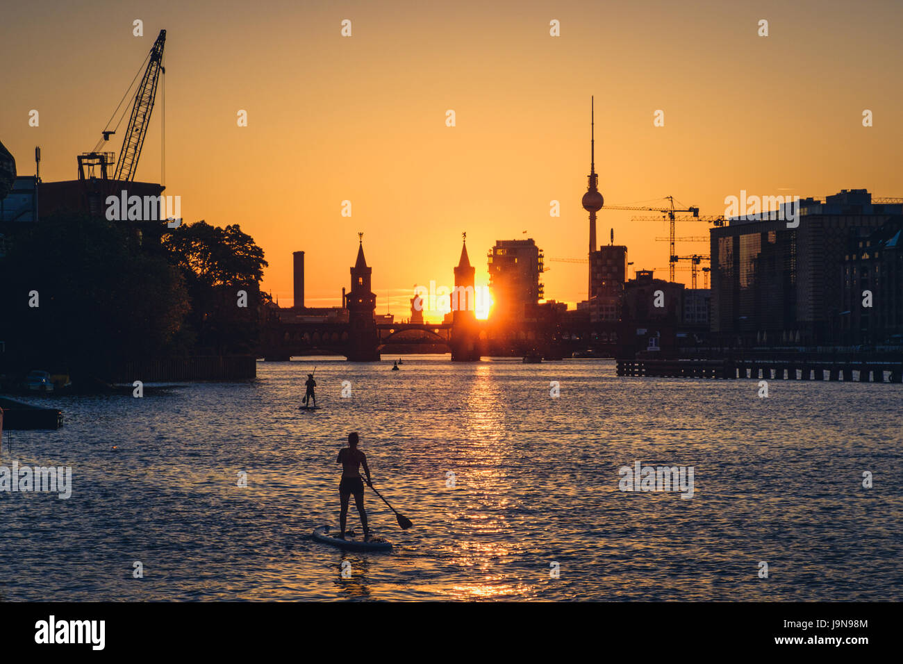Due stand up paddler sul fiume Sprea a Berlino - Ponte Oberbaum, la Torre della TV e del tramonto sullo sfondo del cielo Foto Stock