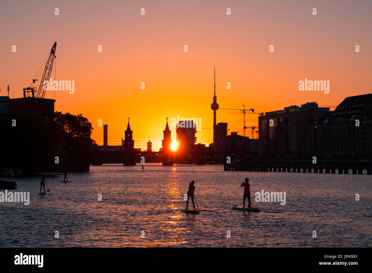 La gente sulla paletta board / stand up paddler sul fiume Sprea a Berlino - Ponte Oberbaum, la Torre della TV e del tramonto sullo sfondo del cielo Foto Stock