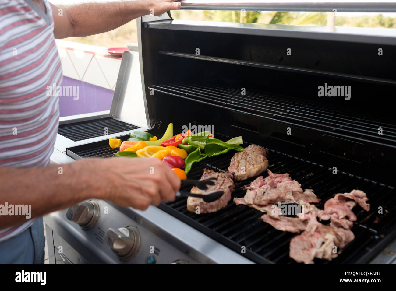 Uomo di bistecca alla brace e diversi tipi di peperone su un grill a gas, close up Foto Stock