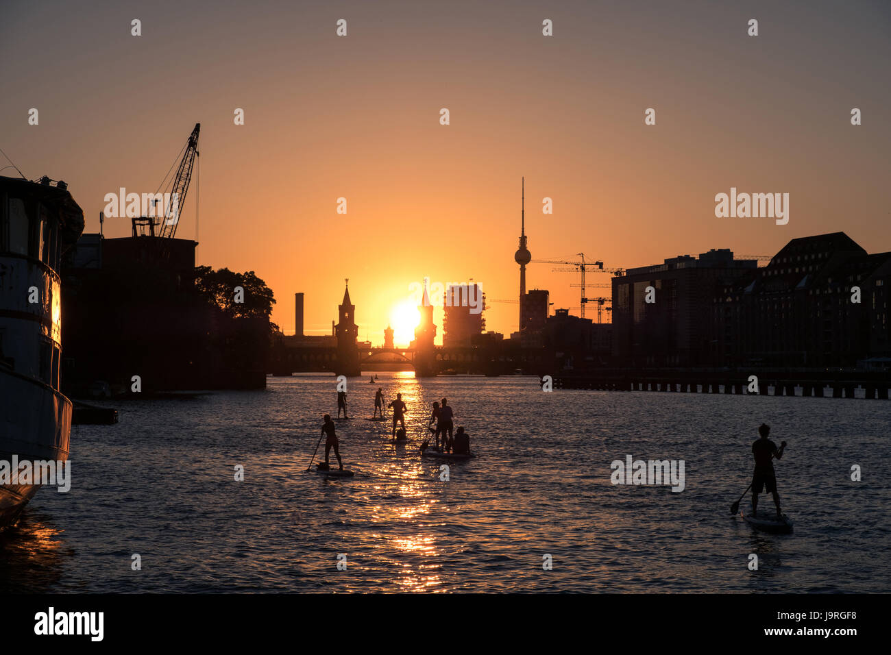 Gruppo di paddle board / stand up paddler sul fiume Sprea a Berlino - Ponte Oberbaum, la Torre della TV e del tramonto sullo sfondo del cielo Foto Stock