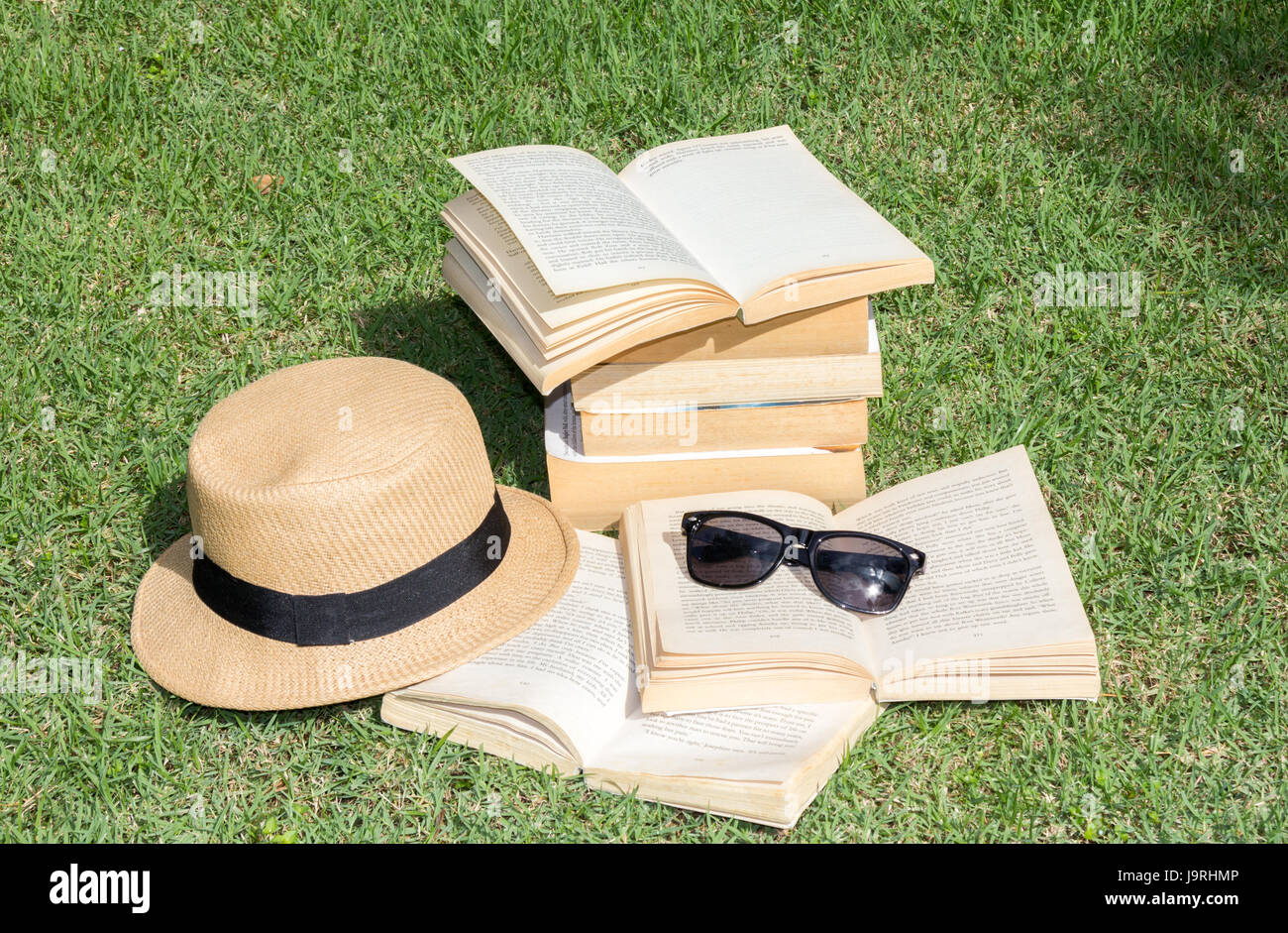 Cappello, occhiali da sole e libri aperti al di fuori di erba Foto Stock
