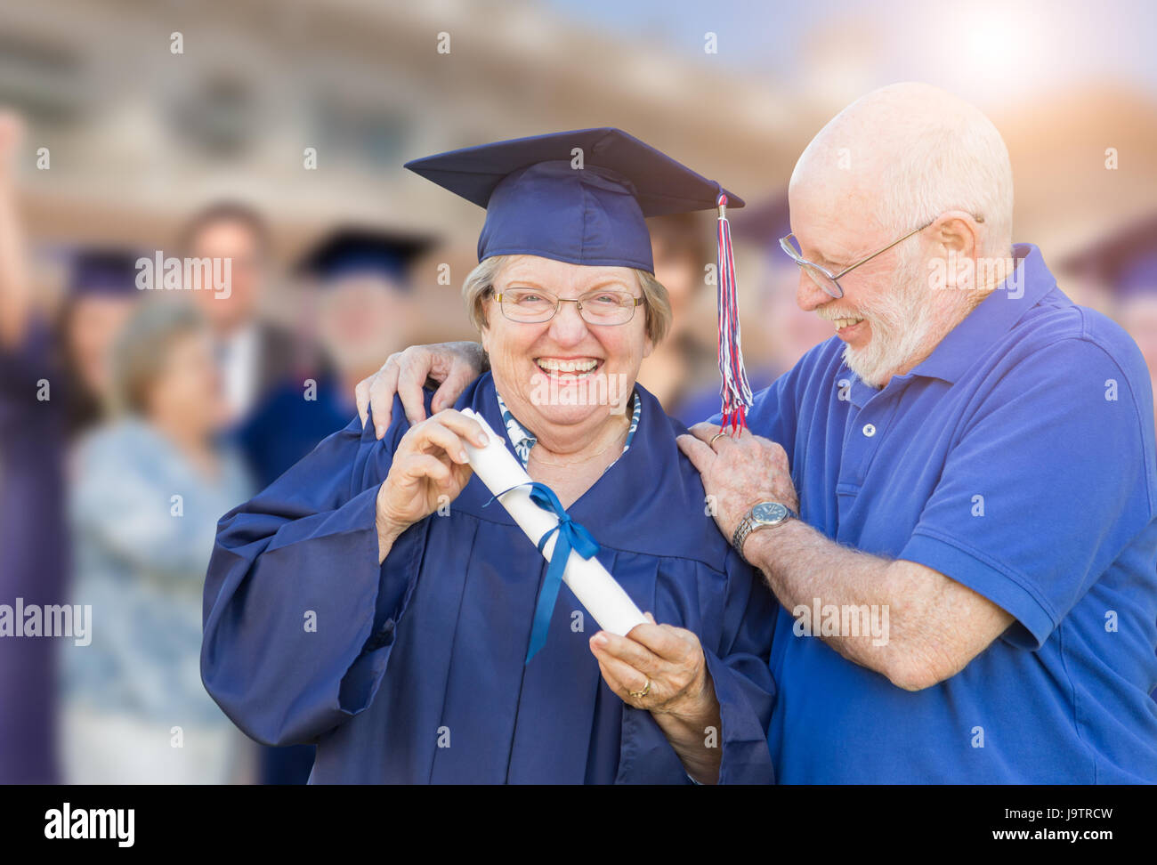 Senior donna adulta nel cappuccio e camice essendo congratulato da marito a Outdoor cerimonia di laurea. Foto Stock