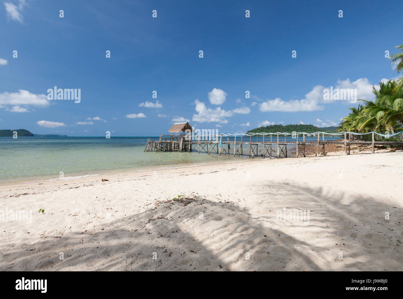 Ombra di noce di cocco con ponte in legno sul mare tropicale. Foto Stock