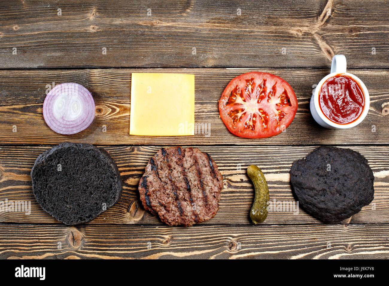 Ingredienti per la cottura di hamburger di nero. Grigliate di carne patty, panini, cipolle, pomodori, lattuga, sottaceti, salsa di formaggio, nero su uno sfondo di legno vista superiore Foto Stock