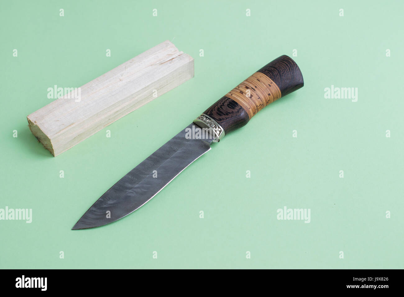 Un coltello realizzato di acciaio di Damasco. Con un manico in legno. Su uno sfondo verde chiaro. Foto Stock