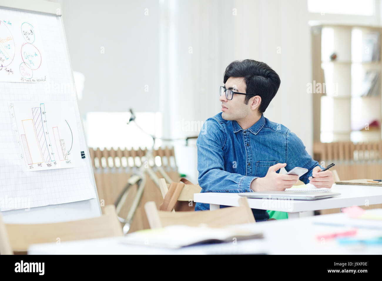 Studente brillante con lo smartphone guardando alla lavagna con grafici e diagrammi Foto Stock
