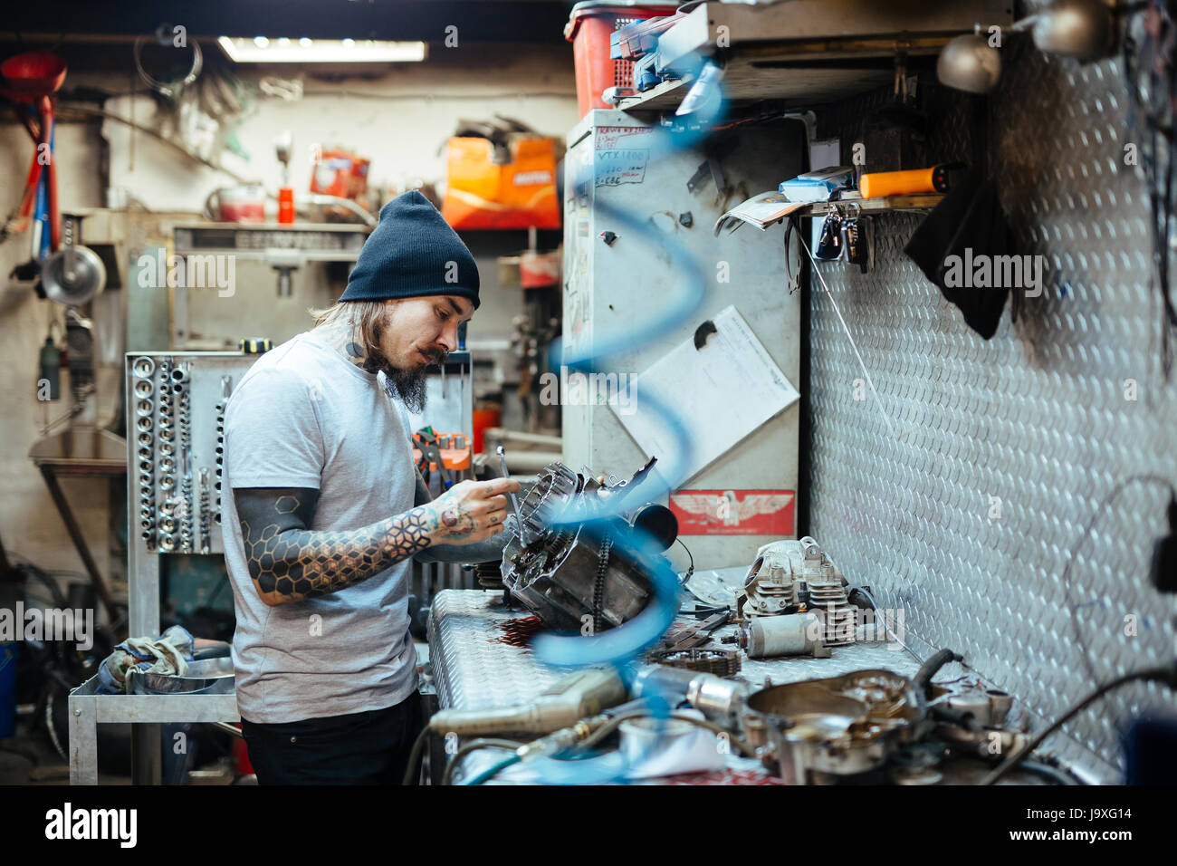 Vista laterale verticale della moderna tatuati l uomo che fissa le parti rotte a tavola in officina Foto Stock