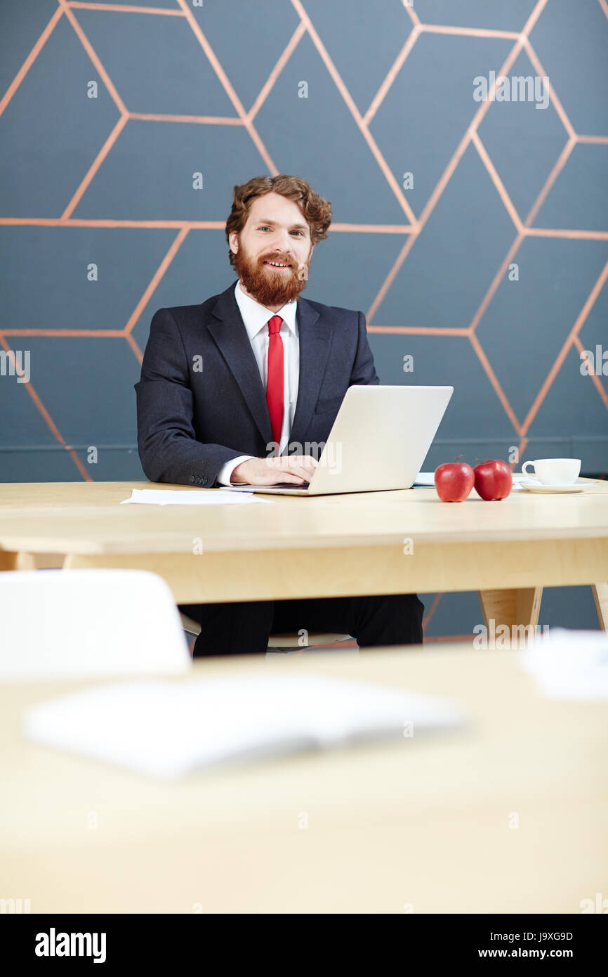 Felice newsreader con laptop seduto da luoghi di lavoro in studio tv Foto Stock