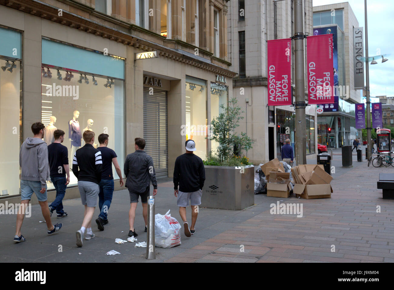 Un folto gruppo di giovani uomini teenage camminare tra i rifiuti e rifiuti shopping sulla strada di Glasgow Foto Stock