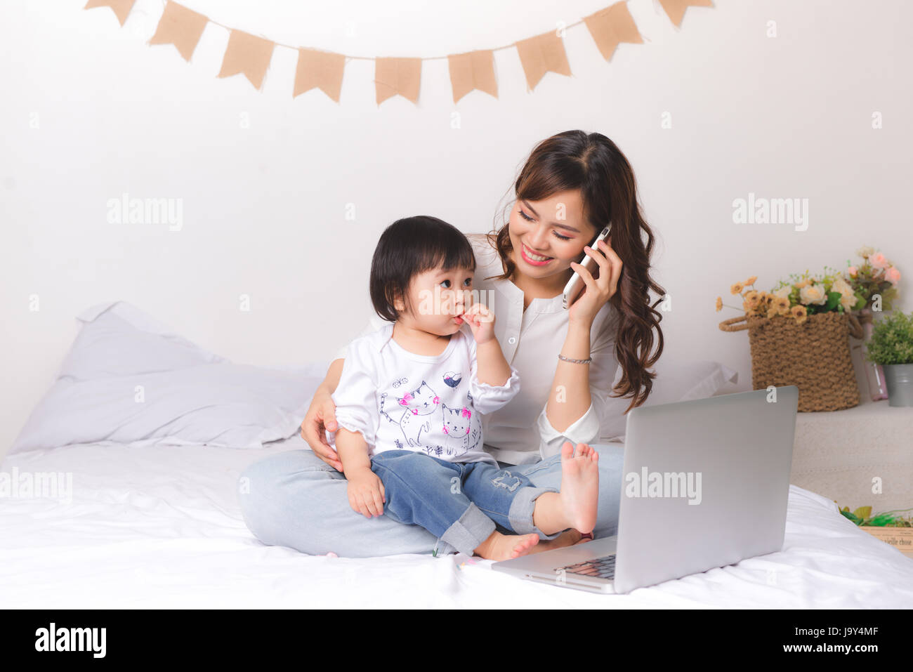 Asian lady in abito classico sta parlando al telefono cellulare e di lavoro sul portatile a casa con la sua bambina. Foto Stock