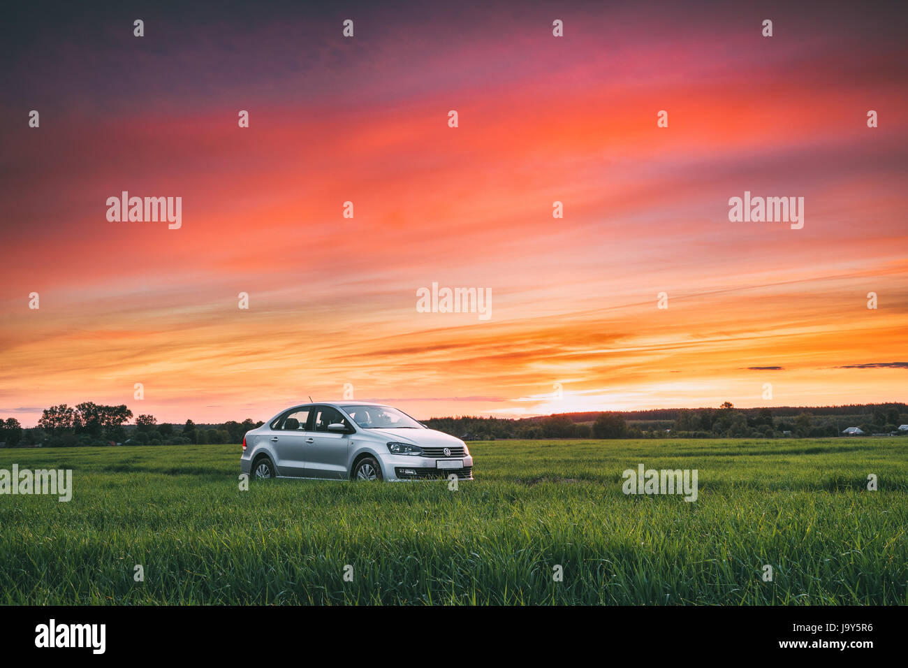 Gomel, Bielorussia - 27 Maggio 2017: Volkswagen Polo Vento berlina auto sulla strada di campagna nella primavera del campo di grano sotto il colorato cielo drammatico al tramonto o l'alba Foto Stock