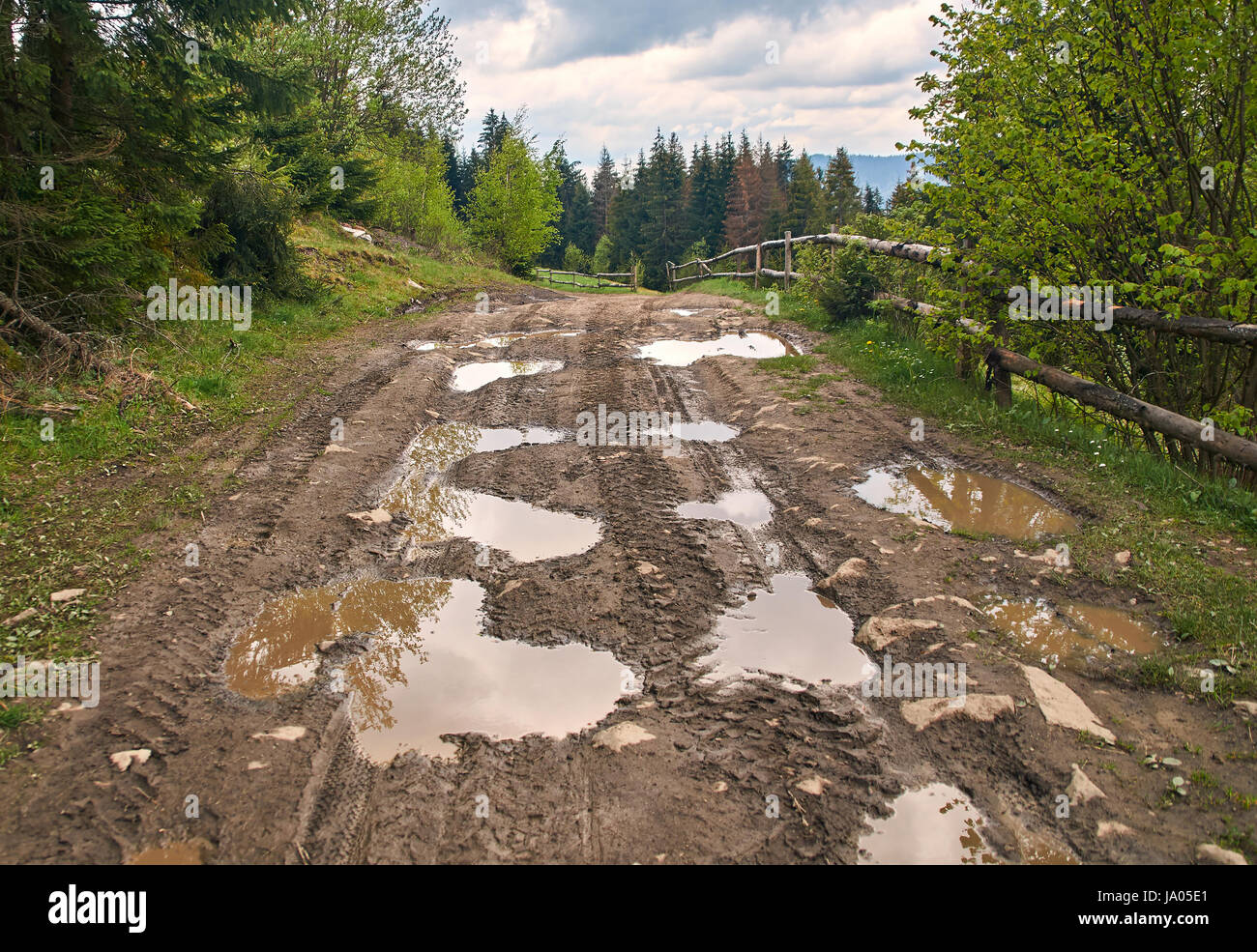 Paese rotto su strada sterrata in primavera montagne con un sacco di pozzanghere fangose dopo la pioggia Foto Stock