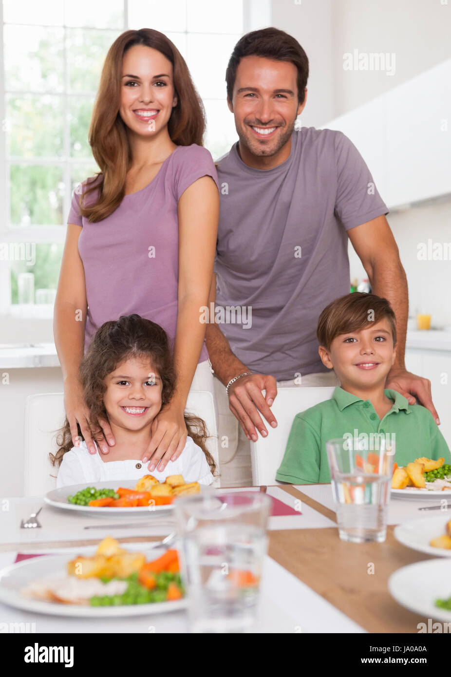 Due bambini e i loro genitori sorridente con la videocamera al tavolo per la cena in cucina Foto Stock