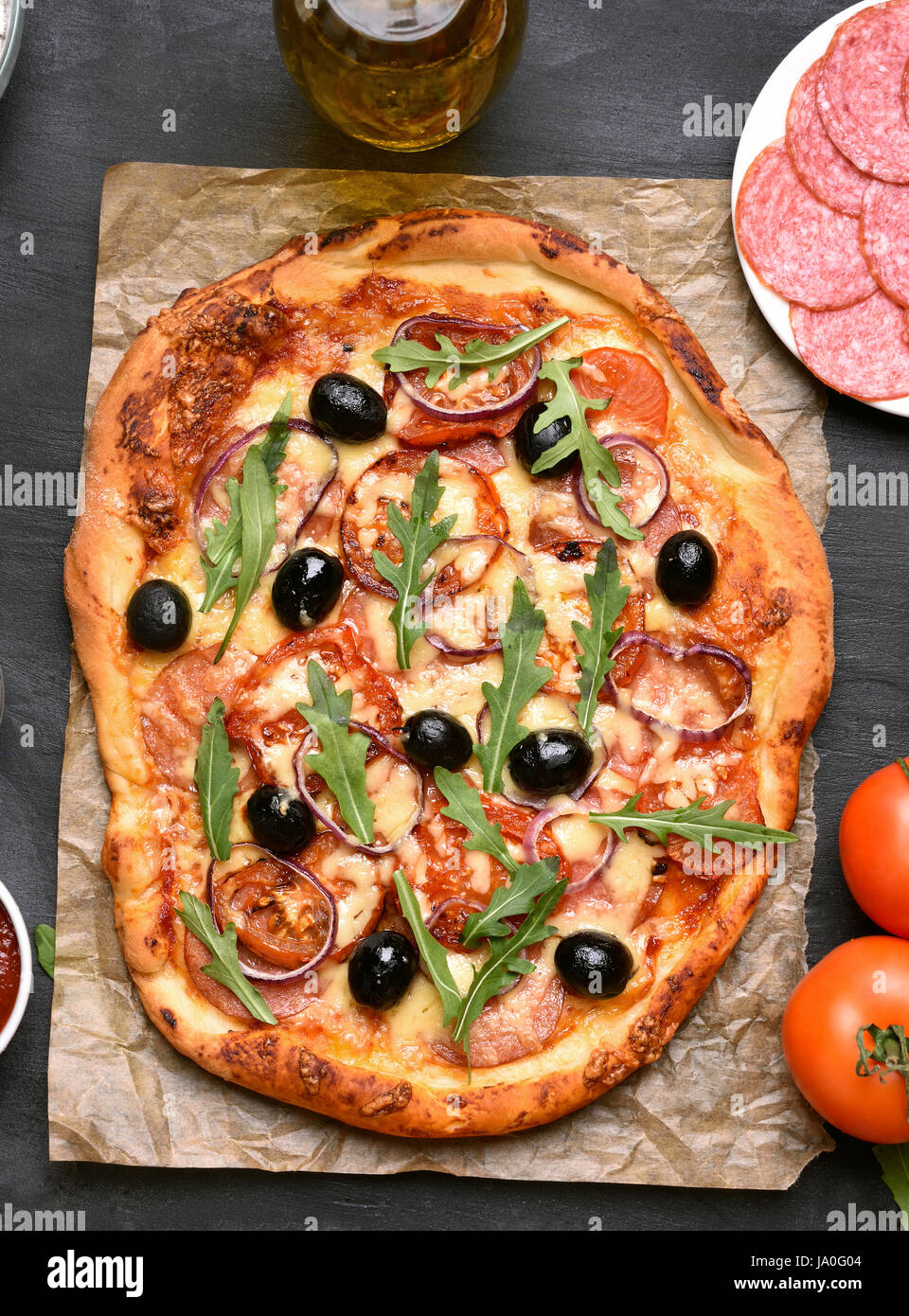 Pizza con pomodoro, salumi e olive su carta su sfondo scuro, vista dall'alto Foto Stock