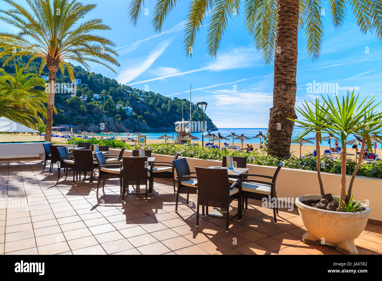 Tavolini da bar terrazza sulla spiaggia con le palme in Cala San Vicente bay, isola di Ibiza, Spagna Foto Stock