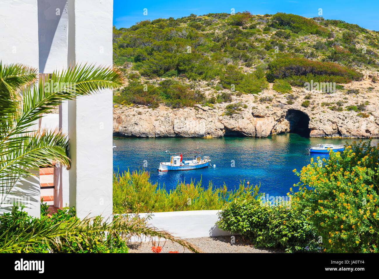 Barca da pesca sul mare di Cala Portinatx bay e la tradizionale casa bianca con Palm tree garden in primo piano, isola di Ibiza, Spagna Foto Stock