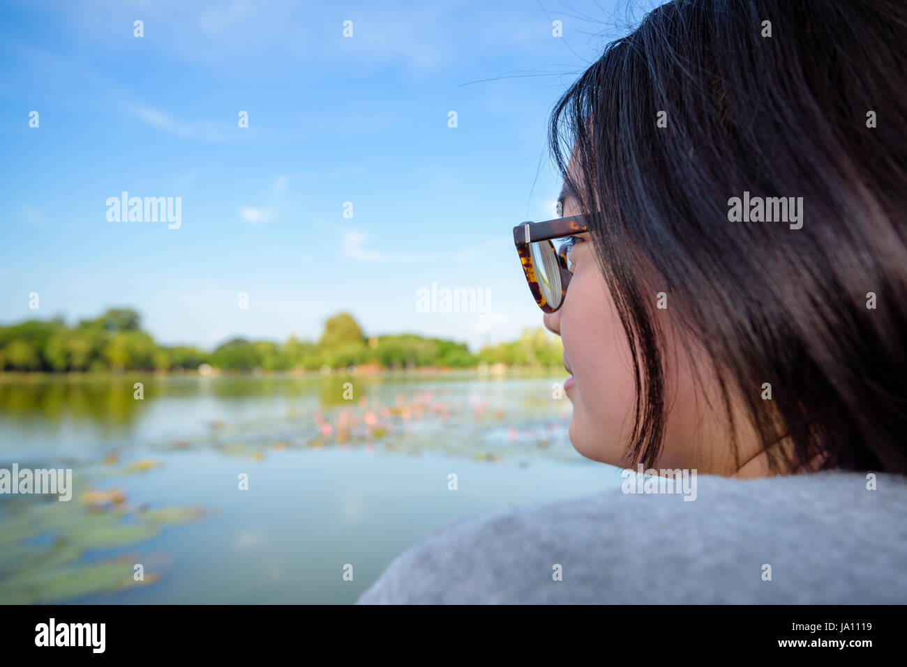 Faccia laterale di una donna che indossa occhiali seduta relax e guardando un paesaggio naturale nei pressi della palude con lotus felicemente Foto Stock