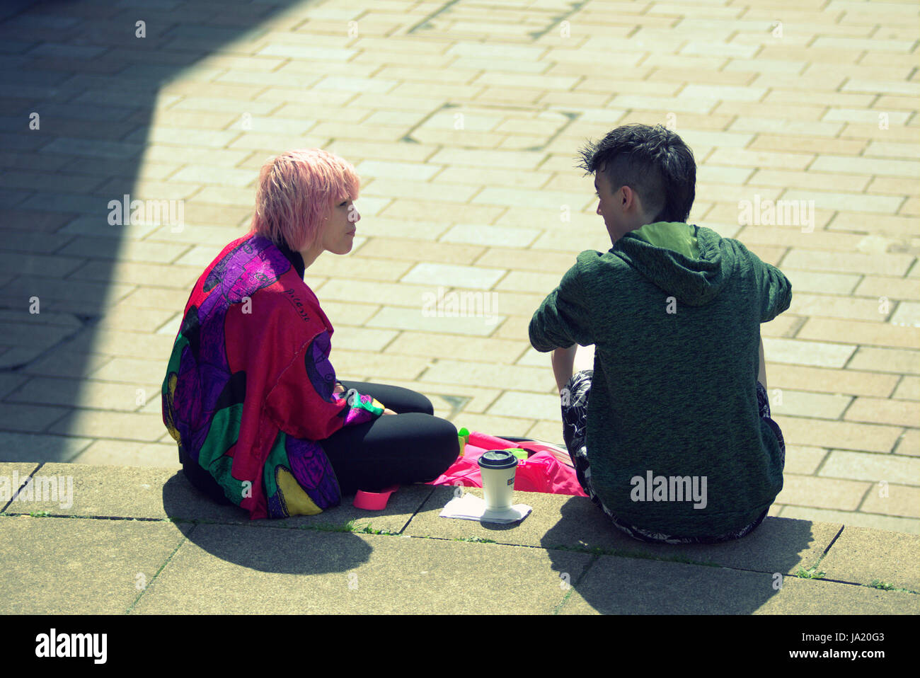 I giovani alla moda un ragazzo e una ragazza colorata parlando seduti sui gradini della sala concerti Glasgow Foto Stock