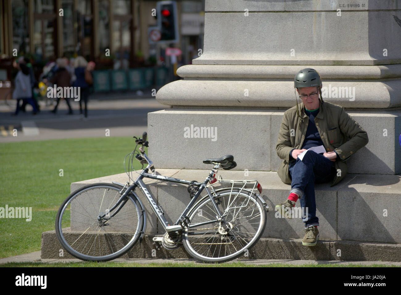 Ciclista seduto mappa di lettura con moto contro il monumento di George Square Glasgow Foto Stock