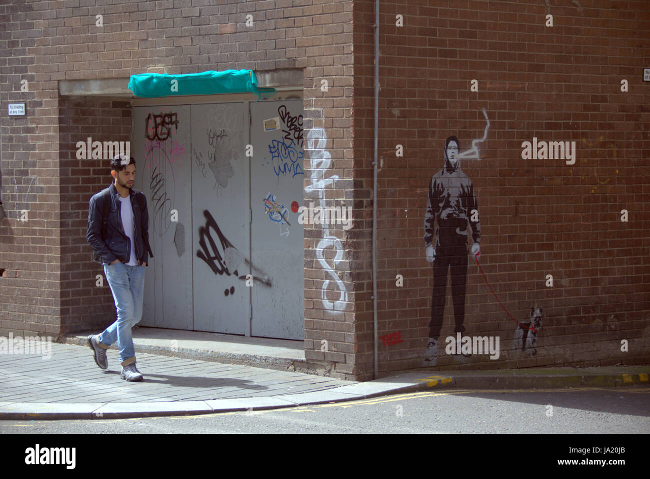 Ragazzo giovane uomo a camminare sulla strada vicino a graffiti di opere d'arte che possono essere viste di progetto circa la sua situazione Foto Stock