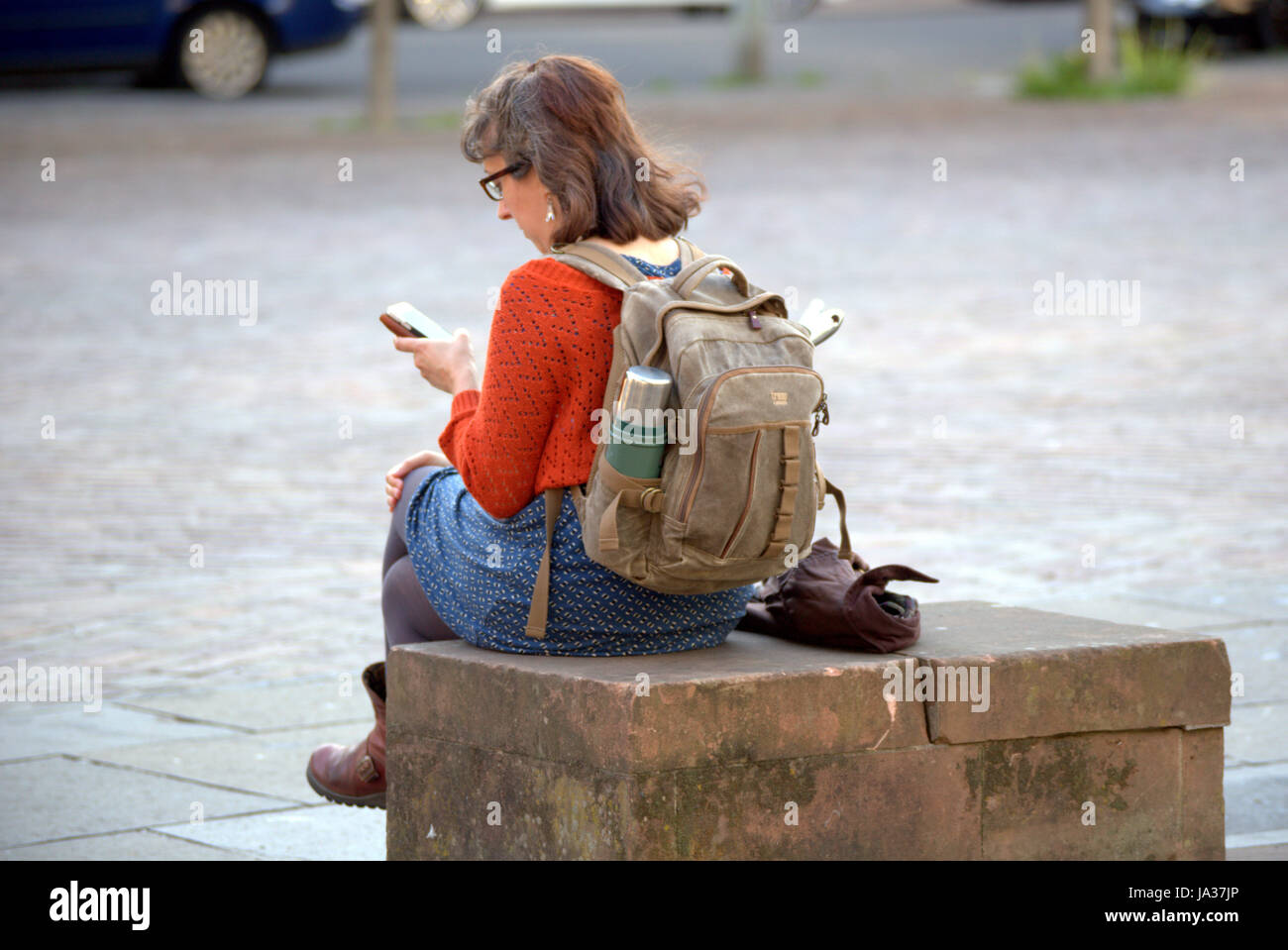 Giovane persona seduta su una panchina visto da dietro utilizzando messaggi di testo sullo smartphone Foto Stock