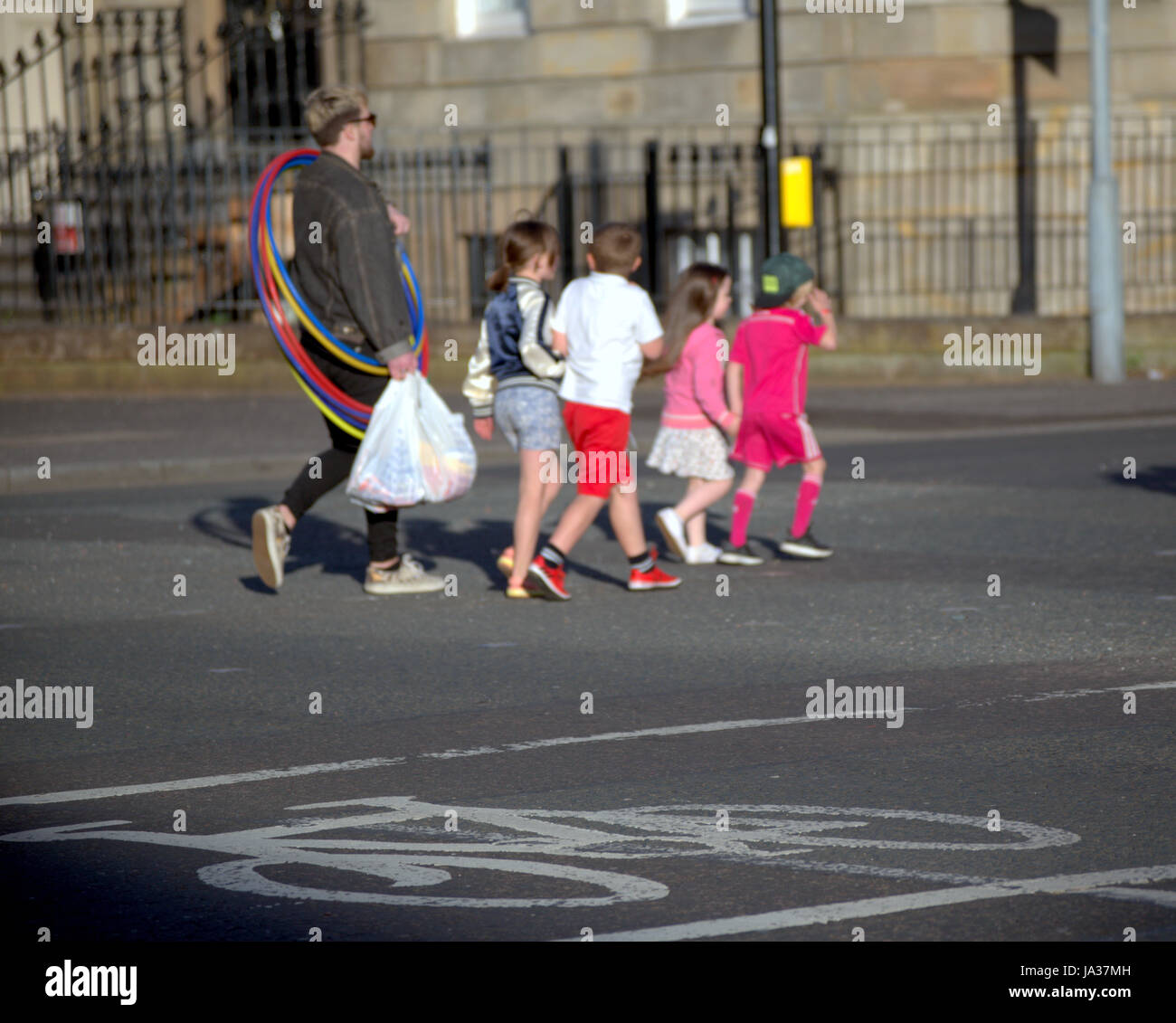 Classe media famiglia bianco fuori a giocare nel parco con padre holding loop di hula attraversando via Foto Stock