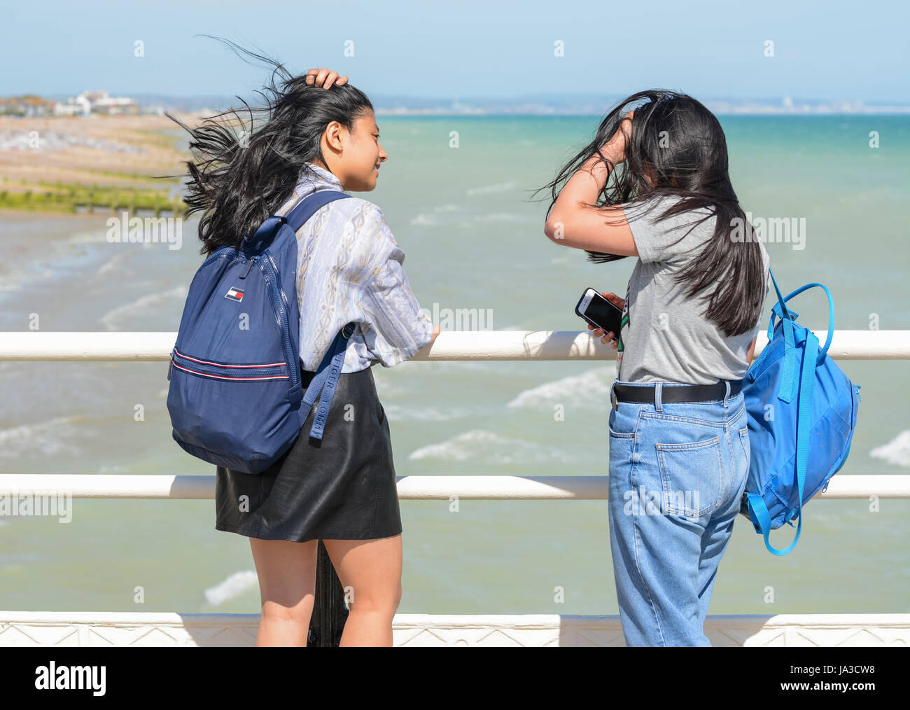 Coppia di adolescenti ragazze asiatiche in piedi nel vento che guarda al mare da un molo. Foto Stock