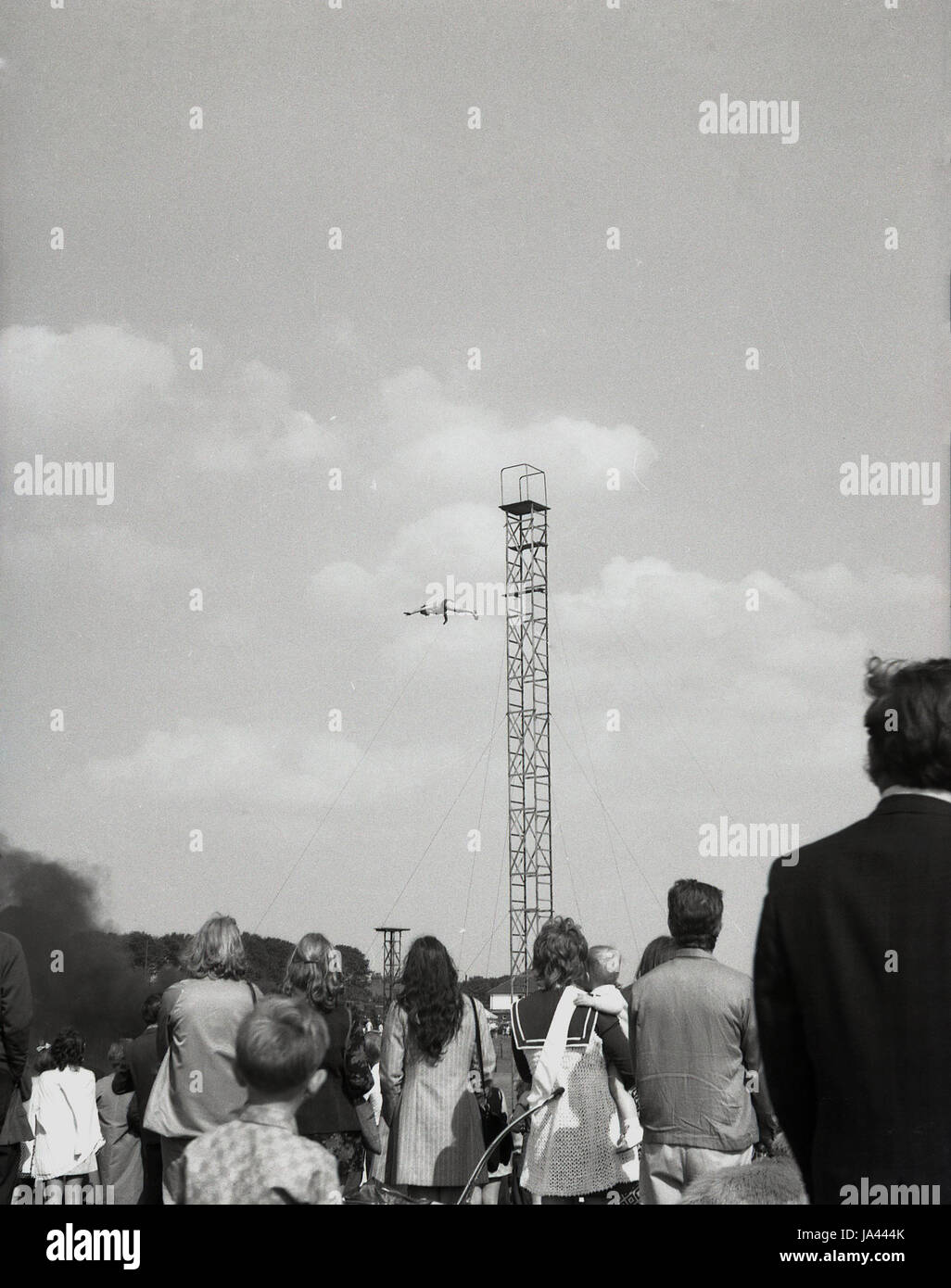 Anni Settanta, Inghilterra, folla guarda come un uomo si tuffa fuori da un alta torre in acciaio in un luna park. Foto Stock