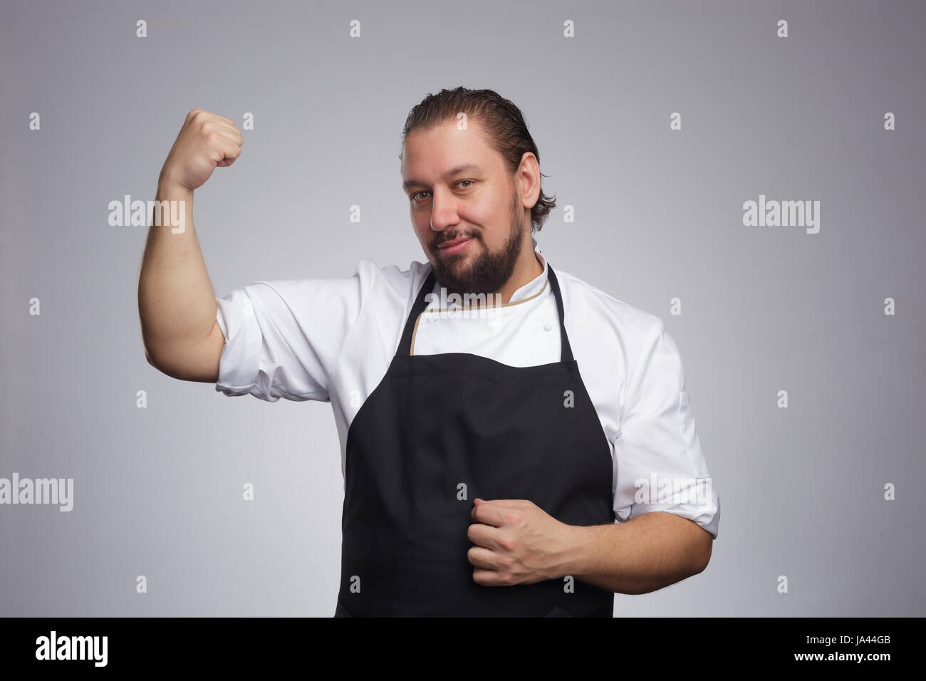 Cuocere in un grembiule nero mostra braccio muscoloso. I risultati di una corretta alimentazione e uno stile di vita sano Foto Stock