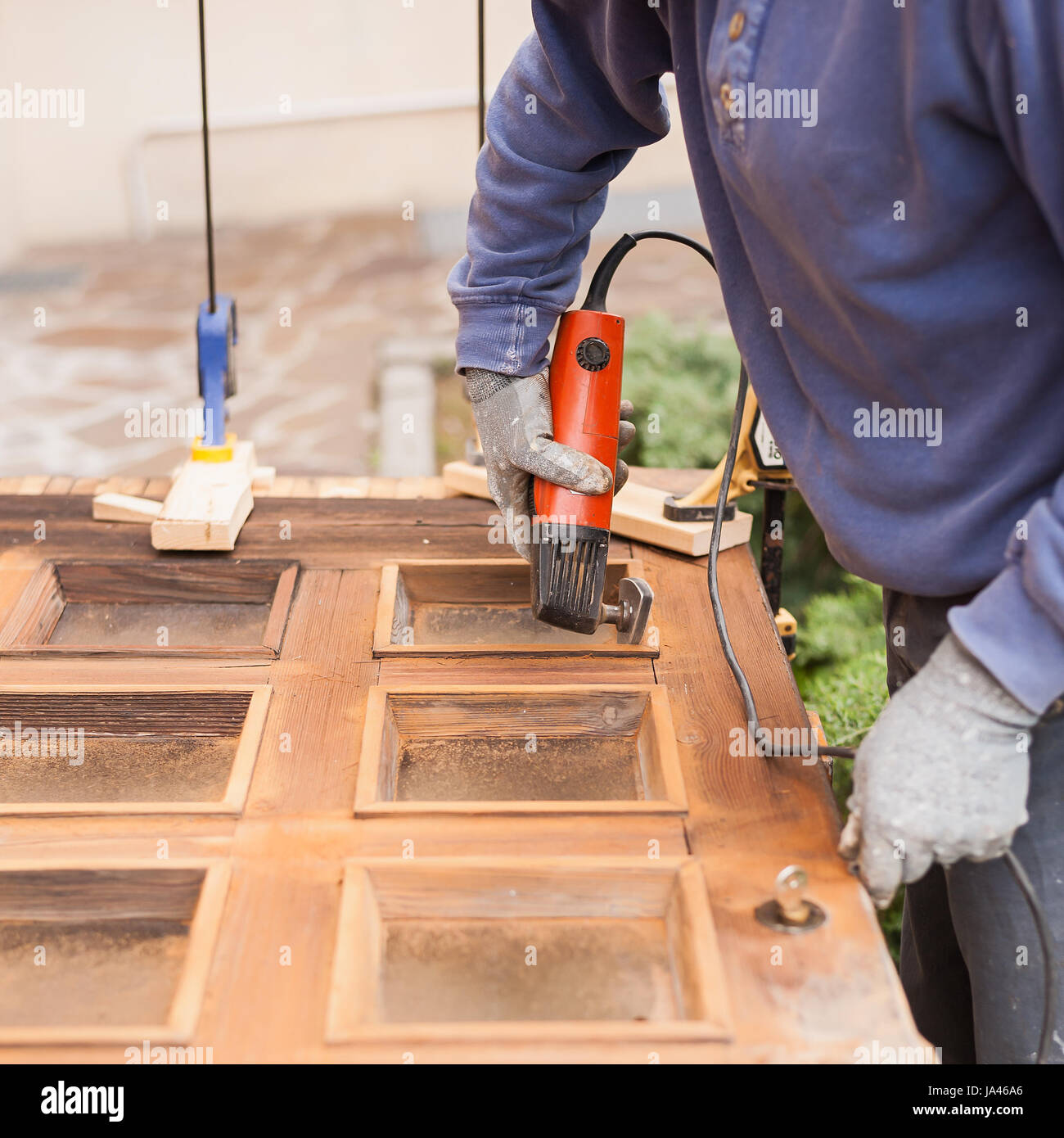 Carpenter al lavoro con la smerigliatrice angolare. La manutenzione e il restauro di una vecchia porta di legno. Foto Stock