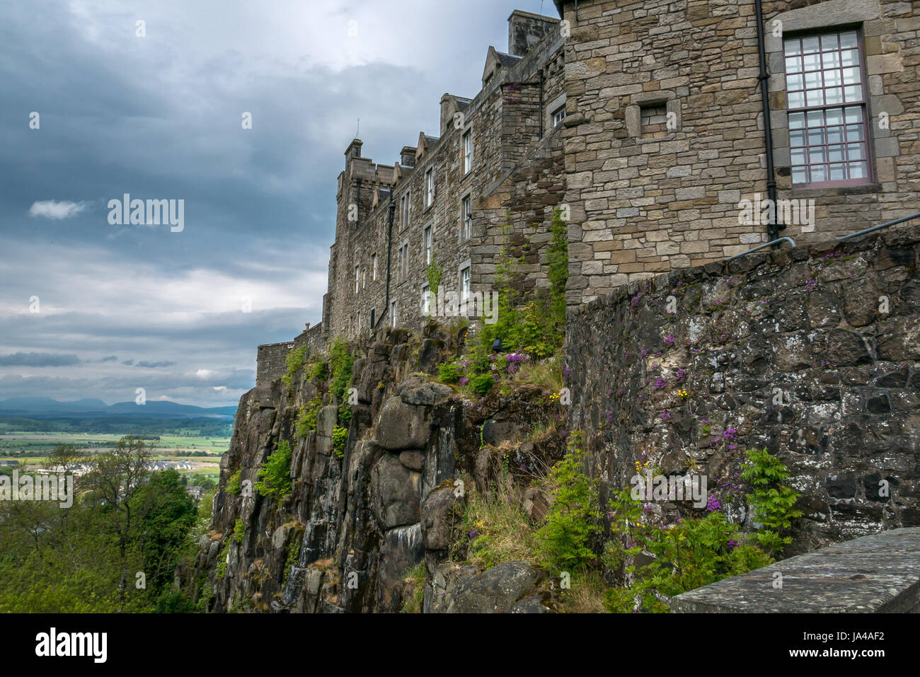 Vista della scogliera rocciosa affioramento con il Castello di Stirling parete e paesaggio distante oltre Carse di Stirling, con moody cielo grigio, Stirling, Scozia, Regno Unito Foto Stock