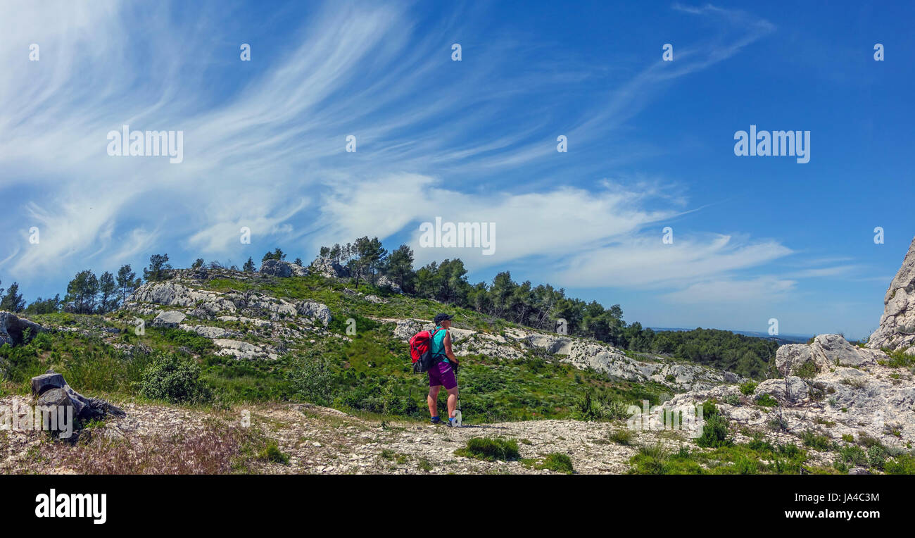 Femmina walker, escursionista in pantaloncini corti, con zaino in spalla e cielo blu con nuvole cirrus Foto Stock