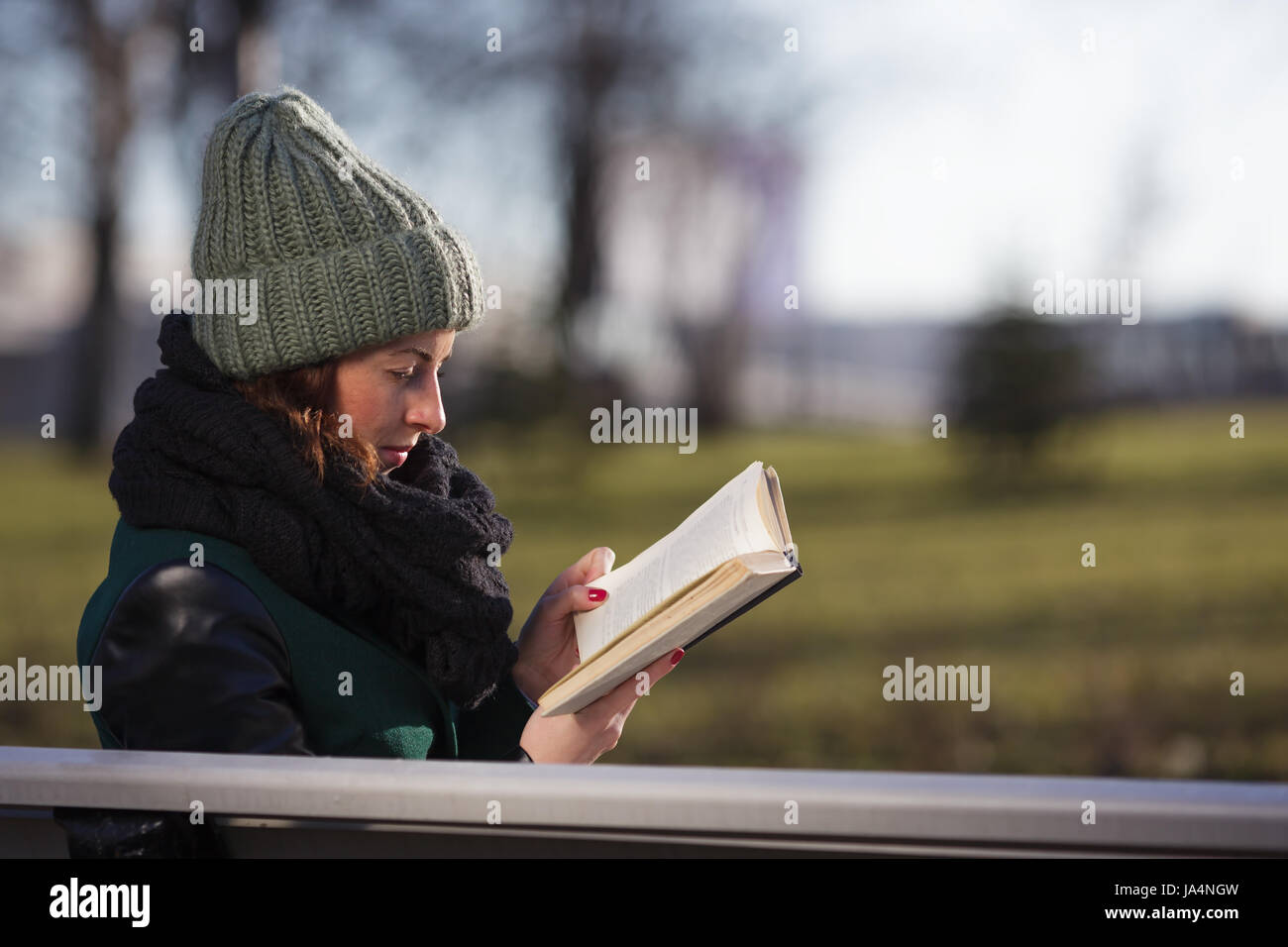 Una ragazza in un cappello si siede su una panchina nel parco e legge un libro. Relax nella natura Foto Stock