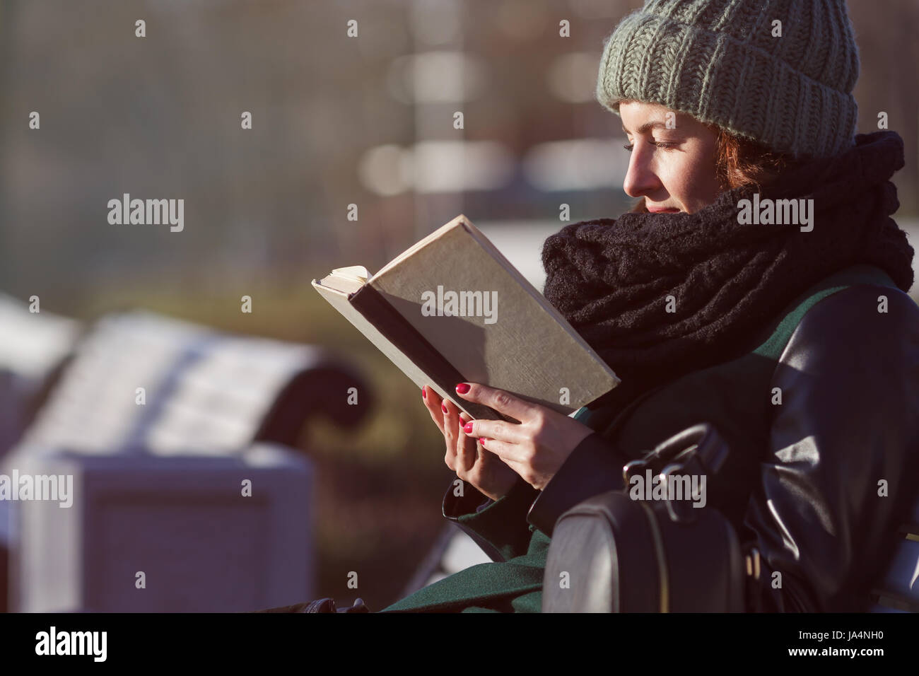 Una ragazza in un cappello si siede su una panchina nel parco e legge un libro. Relax nella natura Foto Stock