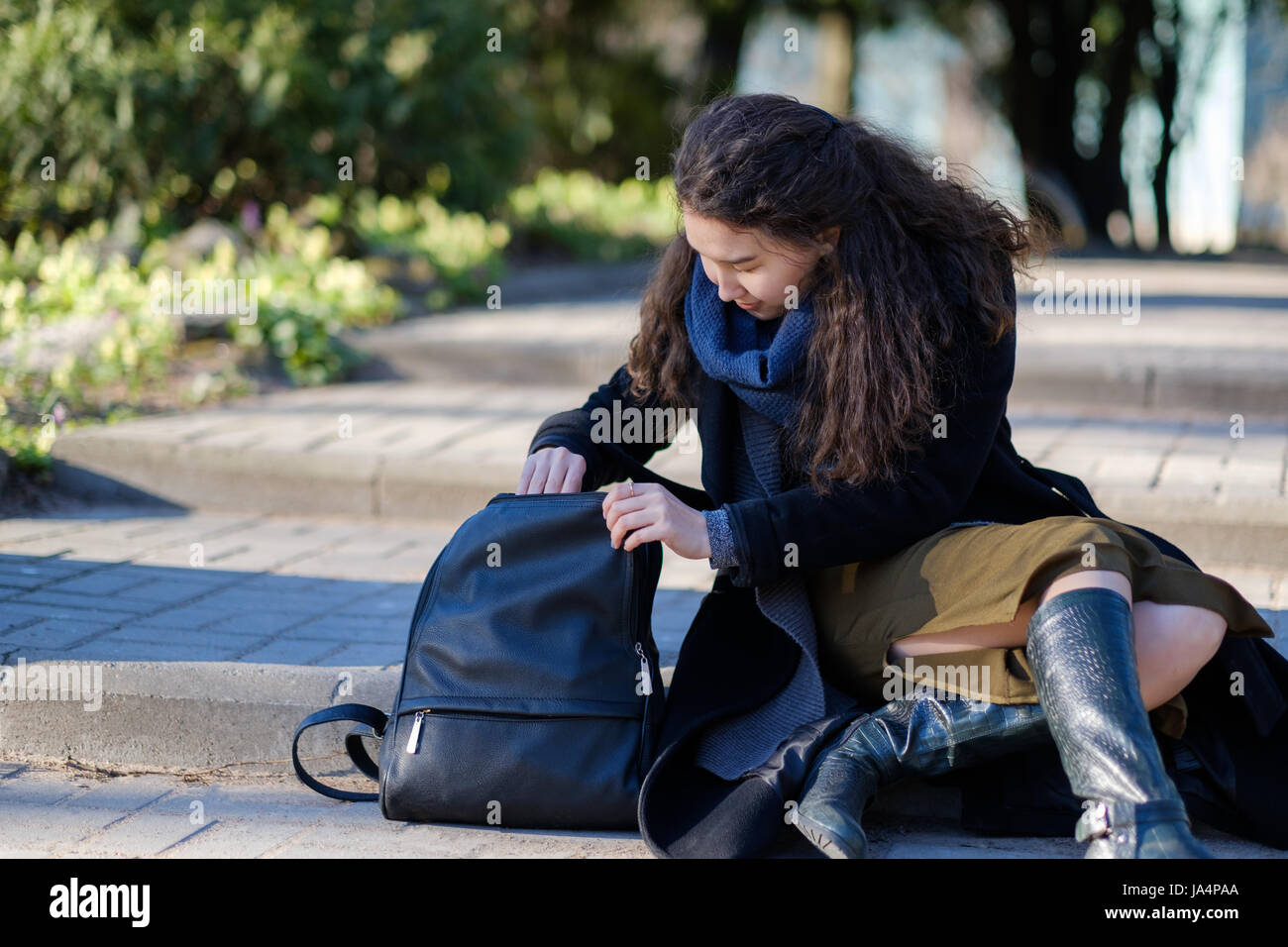 Una ragazza con i capelli lunghi è seduto sui gradini e cercando di trovare le giuste cose nella sua borsa. Foto Stock