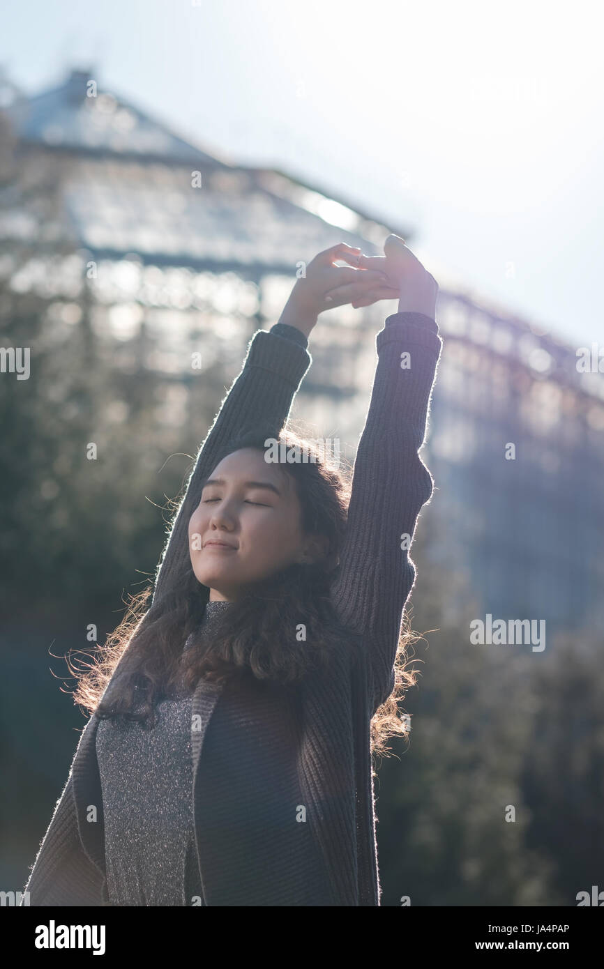 Una bella ragazza asiatica è in piedi nel parco e a riposo crogiolarsi al sole. Godetevi il silenzio nella vita della città. Foto Stock