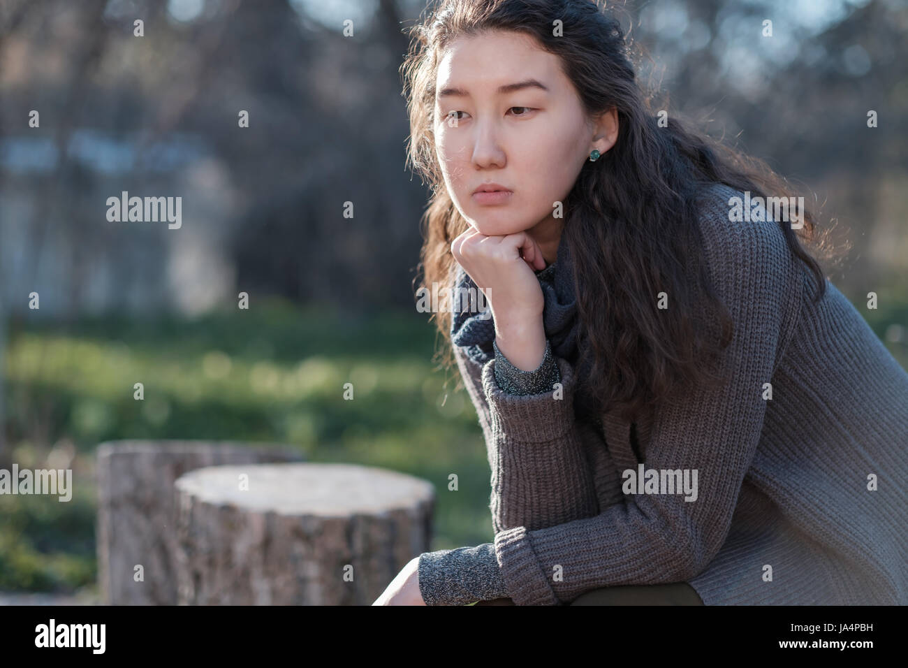 Ritratto di una ragazza asiatica in un parco. Ella si siede da solo e guarda tristemente lontano. Foto Stock