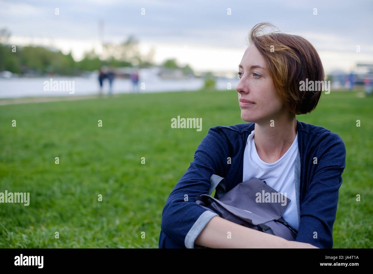 Una ragazza con le lentiggini si siede sul prato verde nel parco. ha uno zaino nelle sue mani. avere un periodo di riposo in estate all'aria fresca. Foto Stock