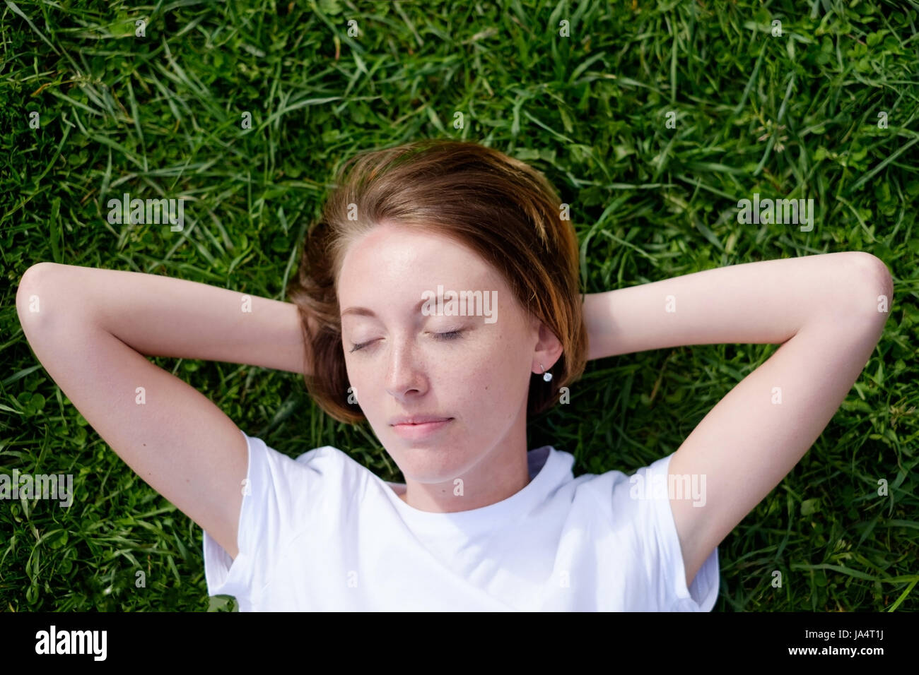 Una bellissima ragazza con le lentiggini giace sull'erba verde con gli occhi chiusi e poggia Foto Stock
