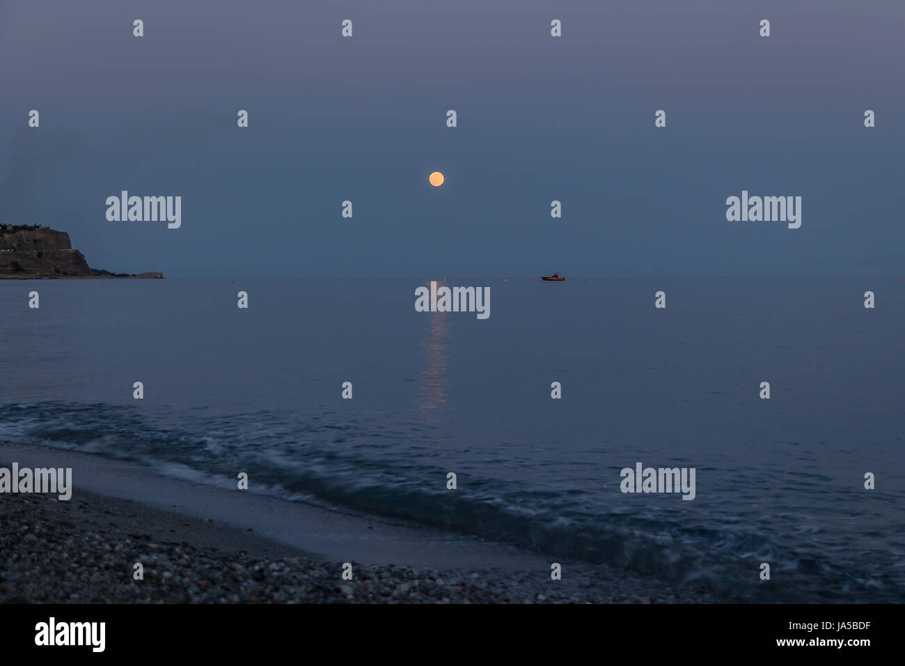 Una barca e la luna che sorge in una spiaggia mediterranea di mare Ionio - Bova Marina, Calabria, Italia Foto Stock