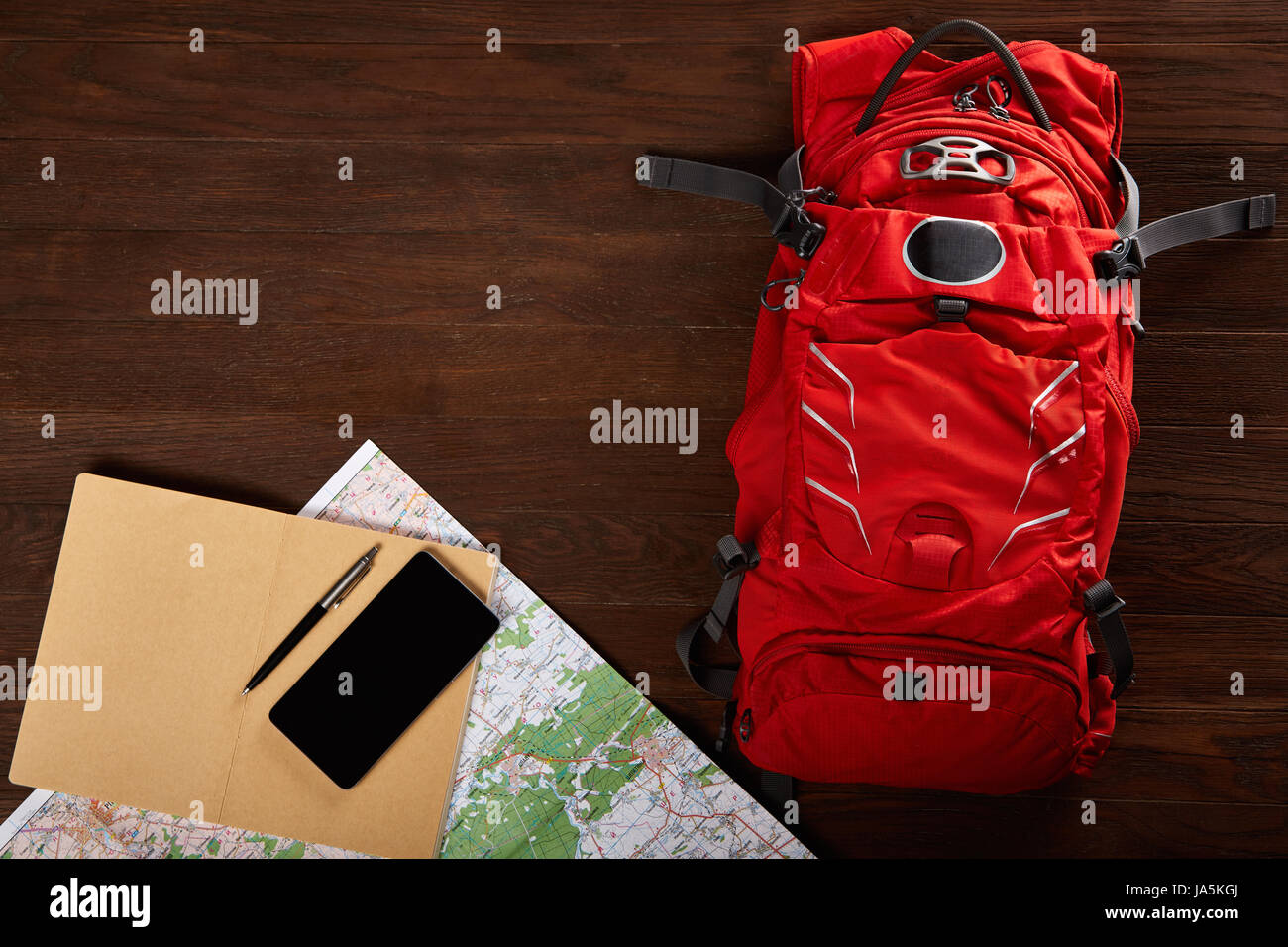 Zaino turistico con mappa, notebook, penna e telefono sullo sfondo di legno. Foto Stock