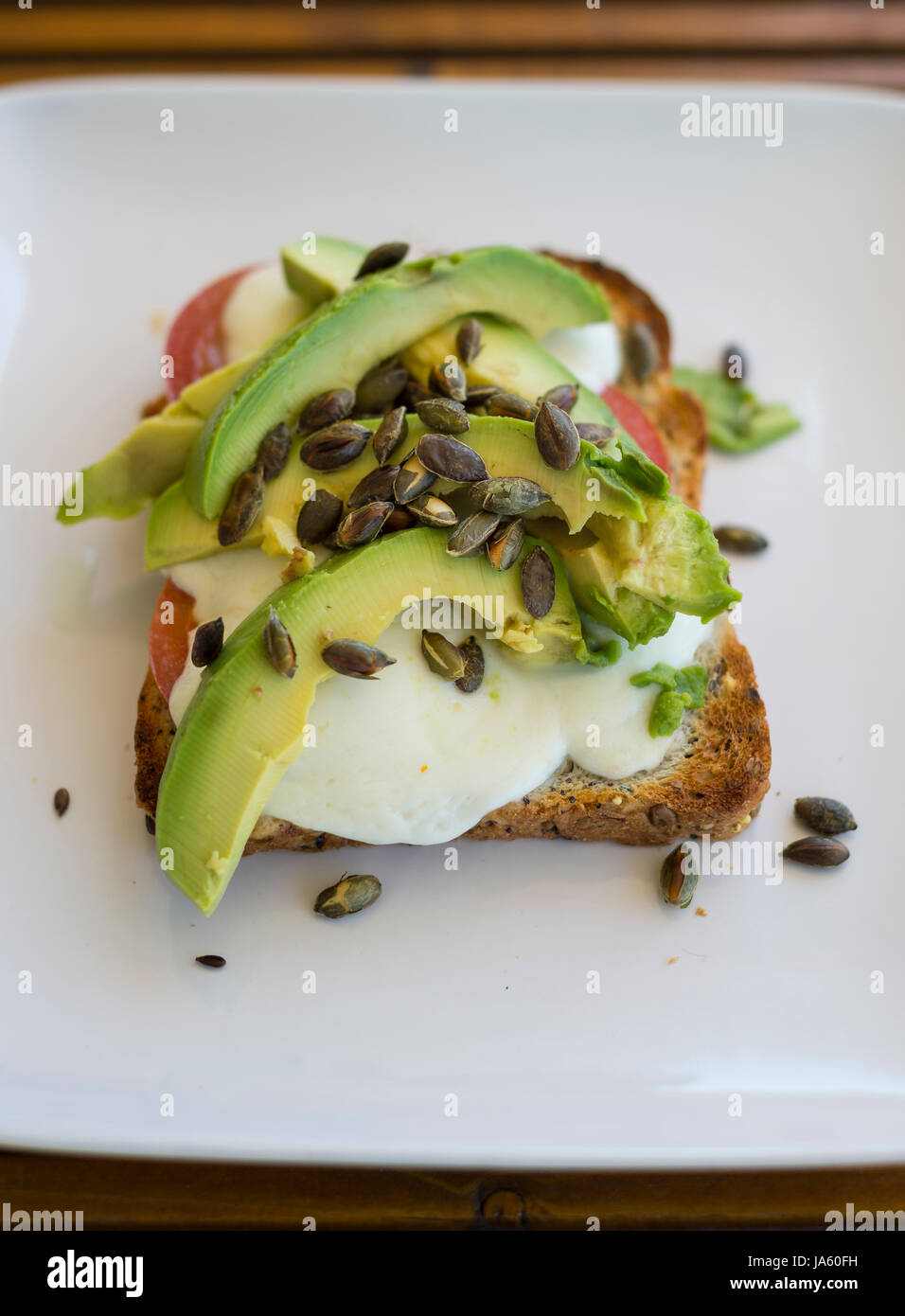 Avocado, mozzarella, pomodoro e tostati Semi di zucca su una fetta di pane tostato integrale Foto Stock